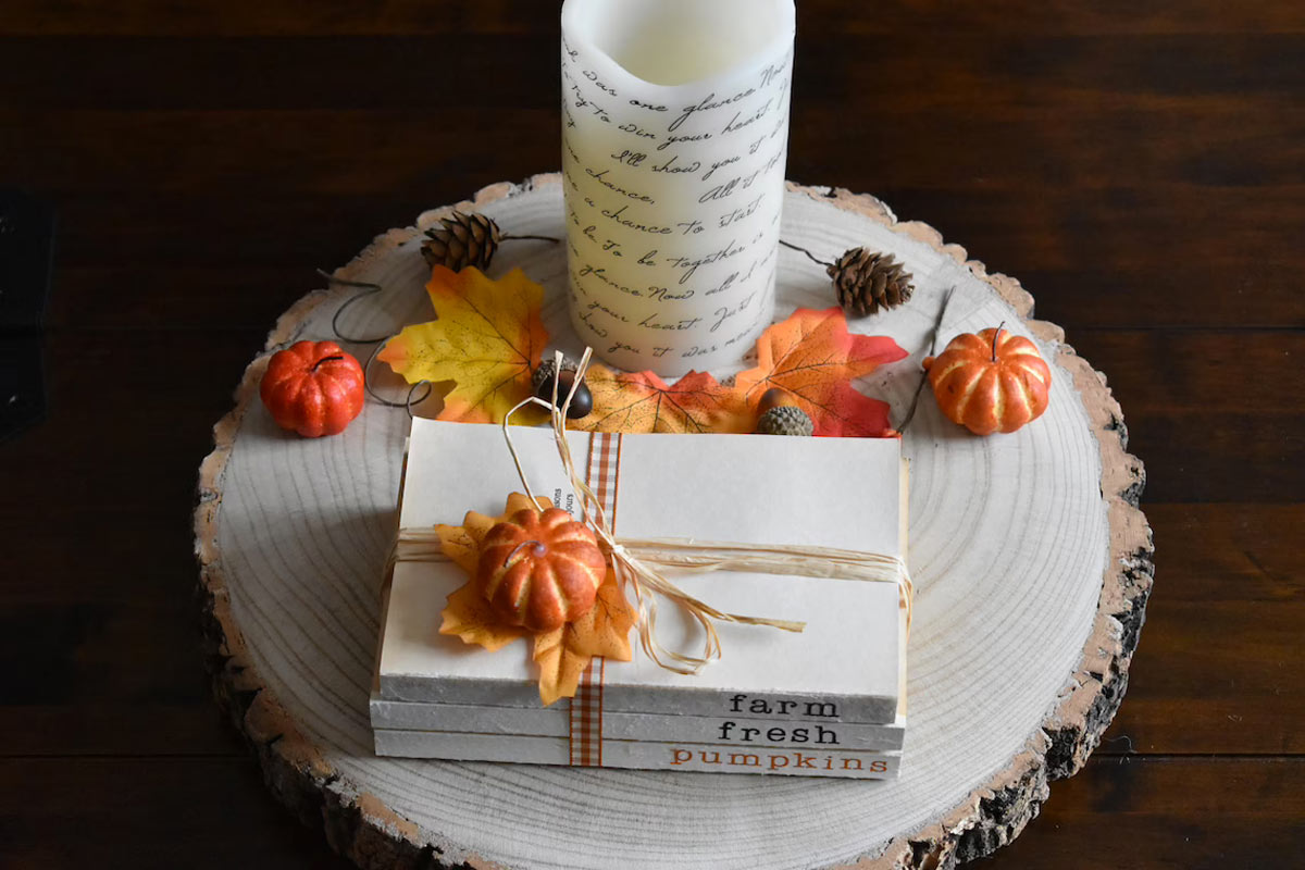 Centrotavola con sezione di legno con candela bianca, foglie secche e piccole zucche, perfetto stile shabby autunnale.